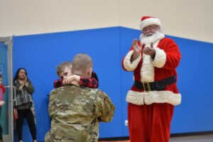 BCMA Student hugging his military father with santa clapping in the background