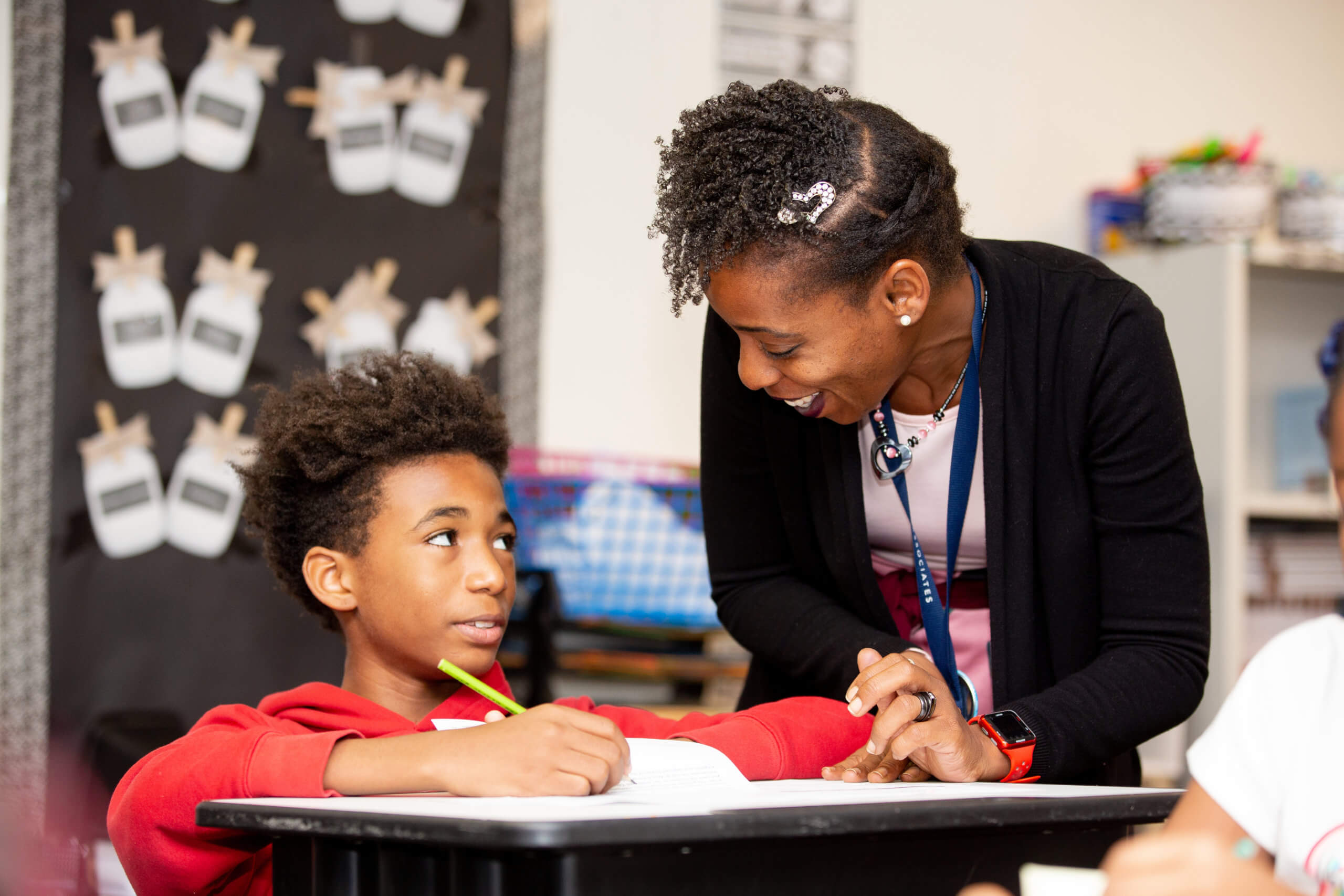 Image of a teacher at Benton Harbor Charter School Academy at a desk with one of her students in the classroom.