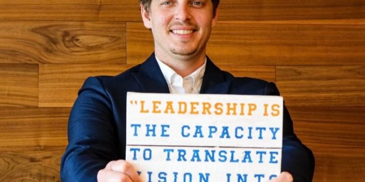 Photo of Alan Bosker Holding a sign with a quote from Warren Bennis that reads, "Leadership is the capacity to translate vision into reality."