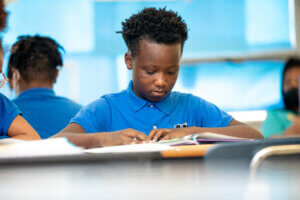 Photo of a student at schools managed by Choice Schools Associates reading in the classroom in their Dove Academy uniform.