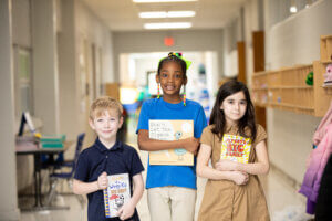 Photo of 3 students at a school managed by Choice Schools Associates holding their favorite books and smiling at the camera.