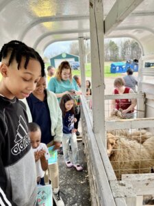 NBCA students celebrate Earth Day with a petting zoo at their campus, picture of students smiling at a goat in the petting zoo.