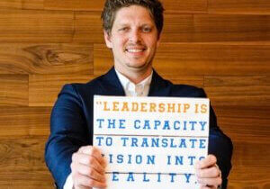 Photo of Alan Bosker Holding a sign with a quote from Warren Bennis that reads, "Leadership is the capacity to translate vision into reality."